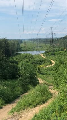 a dirt road in the middle of a lush green field next to a lake and power lines