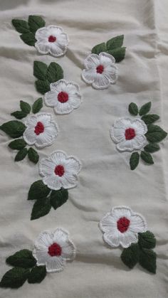 white flowers with green leaves and red centers on a white cloth covered in thread work