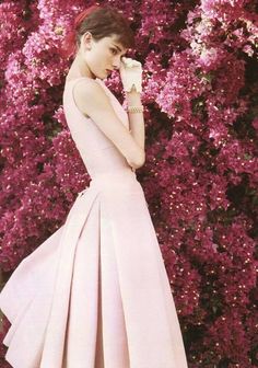 a woman in a pink dress standing next to purple flowers and talking on a cell phone