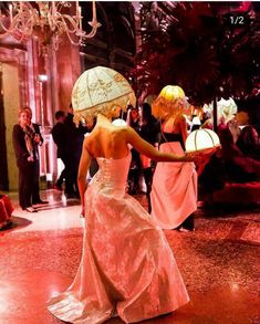 two women in dresses and hats are walking down the hall with an umbrella over their head