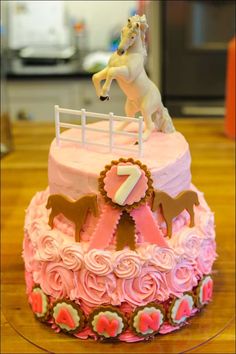 a pink and white cake with a horse riding on it's top is sitting on a table