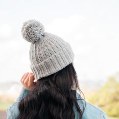 a woman wearing a gray knitted hat with a pom - pom on top