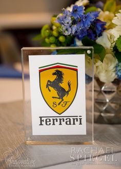 there is a ferrari logo on the glass block next to some blue and white flowers