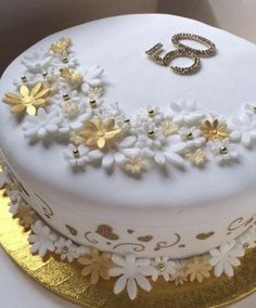 there is a white cake with gold flowers on it, and the number five spelled out