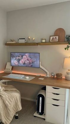 a desk with a computer on top of it next to a lamp and some drawers