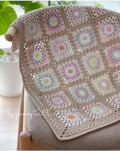 a crocheted blanket sitting on top of a wooden chair next to a potted plant