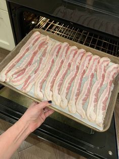 bacon is being cooked in an oven on a pan with a hand reaching for it