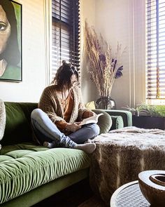 a woman sitting on top of a green couch in a living room next to a window