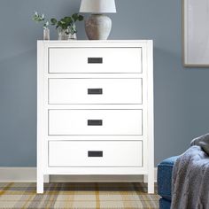 a white chest of drawers sitting in a room next to a blue chair and lamp