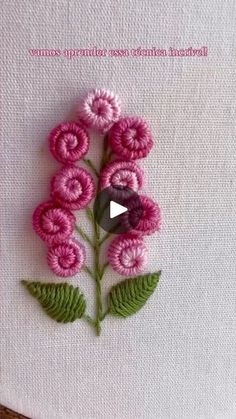 a pink flower with green leaves is embroidered onto a white piece of fabric