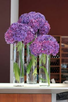 three clear vases with purple flowers in them