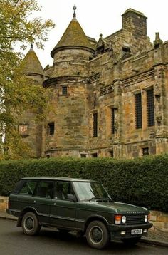 an old car is parked in front of a large stone building with turrets on top