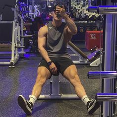 a man sitting on top of a bench in a gym holding a cell phone to his ear