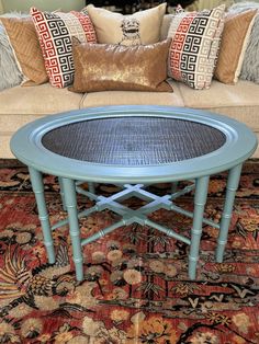 a blue table sitting on top of a rug in front of a couch with pillows