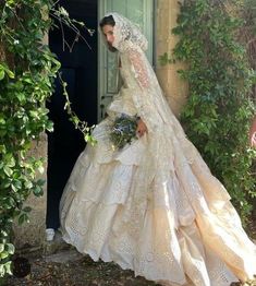 a woman in a wedding dress is standing by a door with greenery around her