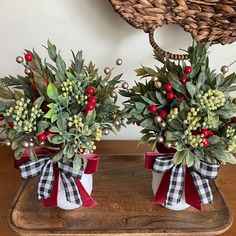 two vases filled with holly and berries on top of a wooden tray next to a wicker basket