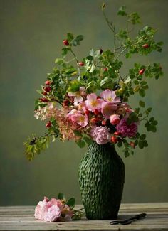 a green vase filled with pink flowers on top of a table