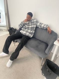 a man sitting on top of a gray couch in front of a mirror and holding his hand to his face