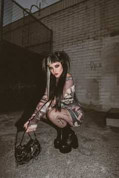 a woman kneeling on the ground next to a black purse and wearing fishnet tights