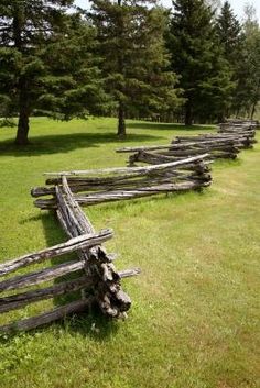 an old wooden fence in the middle of a grassy field with trees and grass behind it