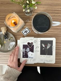 a person holding an open book on top of a table next to a cup of coffee