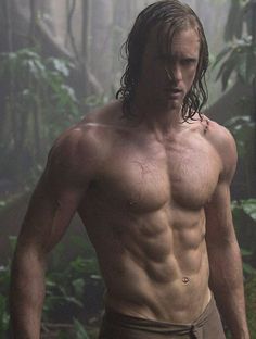 a man with long hair and no shirt standing in the woods