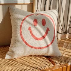 a white pillow with a red smiley face on it sitting on a wicker chair