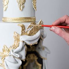 a white and gold wedding cake is being held by a person with a red pencil