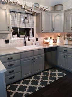 a kitchen with gray cabinets and white counter tops, black and white rug on the floor