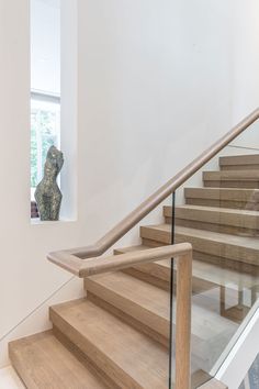 a wooden staircase with glass balustncing and a statue in the window behind it