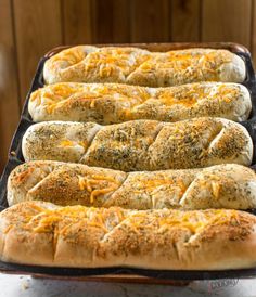 four hot dogs in buns with cheese and herbs on top, ready to go into the oven