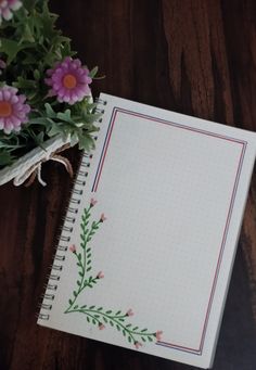 an open notebook with flowers on it sitting next to a potted plant in the background