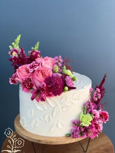 a white cake with pink and green flowers sitting on top of a wooden table next to a blue wall