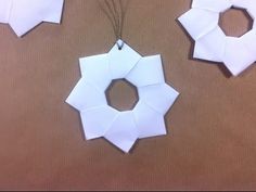 three pieces of white paper are hanging on a brown surface, and one piece is folded to look like a wreath