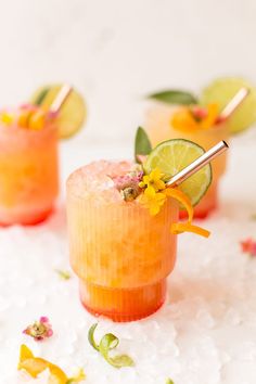 two cocktails with flowers and lime garnish on the rim, sitting on ice