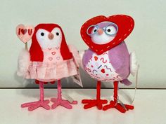 two stuffed birds are standing next to each other with hearts on their heads and beaks