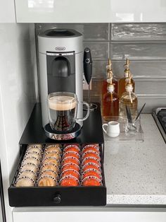 an espresso machine and some cookies in a tray on a counter top next to bottles of alcohol