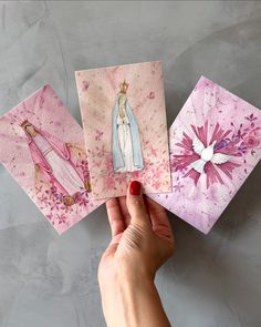 a hand holding three cards with pictures of the virgin mary