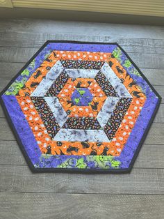 an orange, purple and black patchwork table topper on a wooden floor next to a window