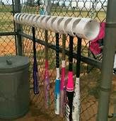 several baseball bats are hanging on a chain link fence near a trash can and garbage can