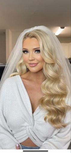 a woman with long blonde hair wearing a wedding veil and posing in front of the camera