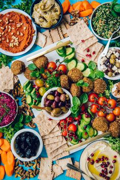 an assortment of food on a platter with crackers, olives, tomatoes, cucumbers and more