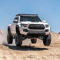 a white toyota truck driving on top of a dirt hill in the middle of nowhere