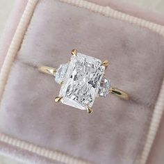 a cushion - cut diamond ring sits on top of a pink velvet box, with two diamonds in the band