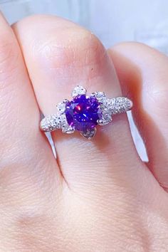 a woman's hand holding a ring with a purple stone and diamonds on it