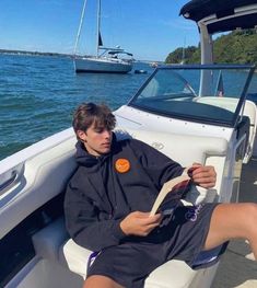 a young man sitting on the back of a boat reading a paper while wearing shorts