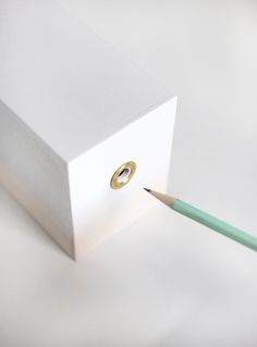 a pencil sticking out of a white box with a gold ring on it's end