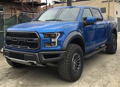 a blue truck is parked in front of a fenced off area and some buildings