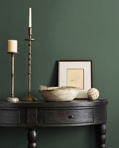 a table with a bowl and candles on it in front of a green painted wall