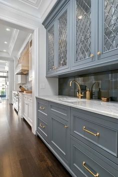 a kitchen with gray cabinets and gold pulls on the handles, white marble countertops and wood flooring